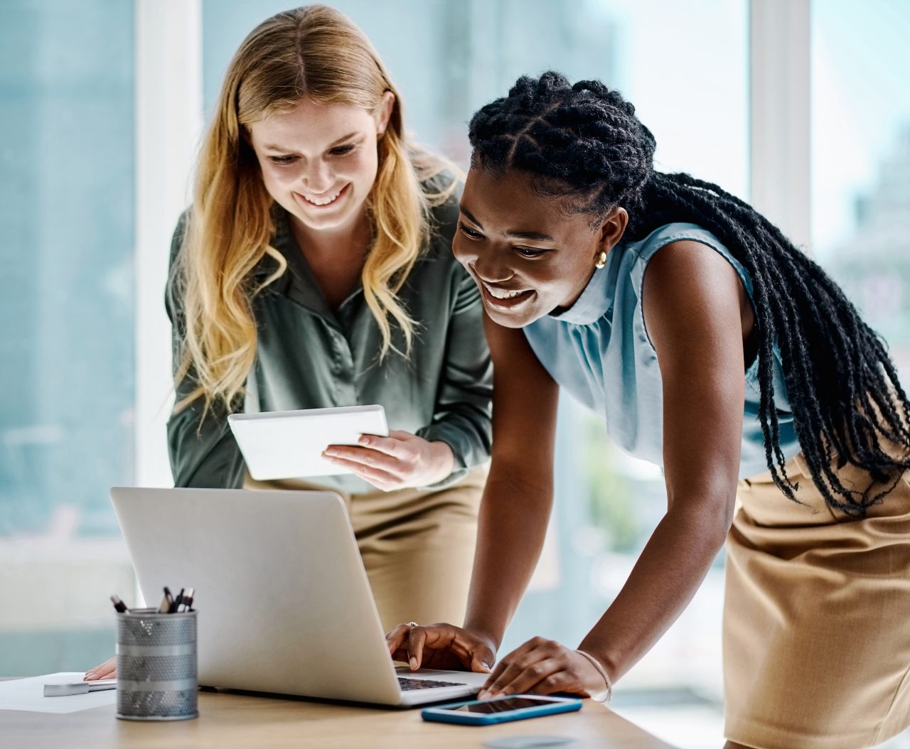 Two diverse businesswomen working together on a digital tablet and laptop in an office