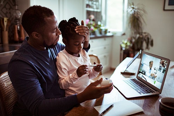 man and child video chatting with doctor on laptop