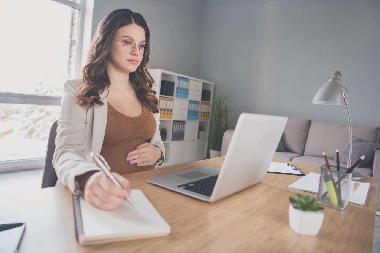 Photo of pregnant manager look netbook screen write diary wear suit brown shirt workstation office indoors.